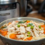 Bowl of slow cooker chicken noodles with tender chicken, thick noodles, and veggies in a creamy broth